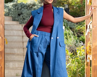 May include: A woman wearing a long denim vest over a burgundy turtleneck top and matching denim pants. The vest has a double-breasted closure and pockets. The pants have a drawstring waist and cuffed legs.