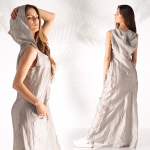 May include: A sleeveless linen dress with a large hood. The dress is a light gray color and has a relaxed fit. The model is wearing the dress with a casual, relaxed look.