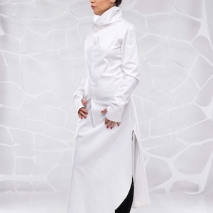 May include: A white long-sleeved shirt with a high collar and a long, flowing hem. The shirt has a side slit and is worn with black leggings and black shoes.