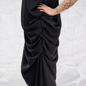May include: A black, flowing, draped dress with a gathered, asymmetrical hemline.