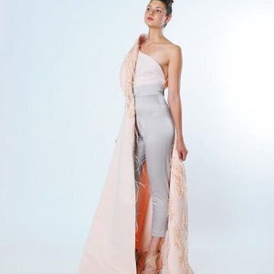 May include: A woman wearing a gray jumpsuit with a pink and peach feathered cape. The cape is draped over one shoulder and has a long train.