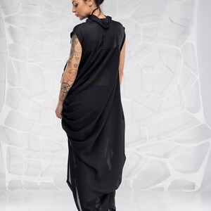 May include: A black sleeveless dress with a draped design. The dress is made of a sheer fabric and has a high neckline. The model is wearing black heels.
