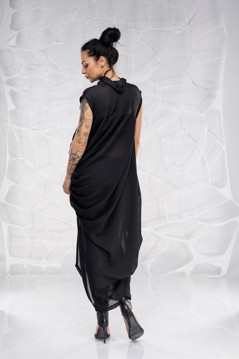 May include: A black sleeveless dress with a draped design. The dress is made of a sheer fabric and has a high neckline. The model is wearing black heels.