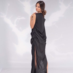 May include: A sleeveless black dress with a high neckline and a draped, asymmetrical design. The dress features a high slit on one side and is paired with black high heels with red soles.