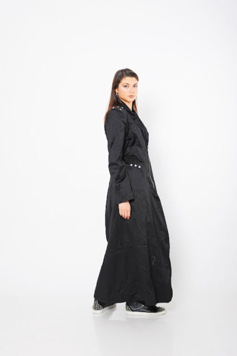 May include: A long black coat with a zipper closure and silver accents. The coat has a fitted bodice and a flowing skirt.