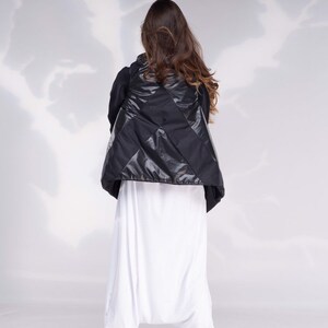 K&ouml;nnte beinhalten: Eine schwarze gesteppte Weste mit Rautenmuster. Die Weste wird &uuml;ber einer wei&szlig;en Hose getragen.