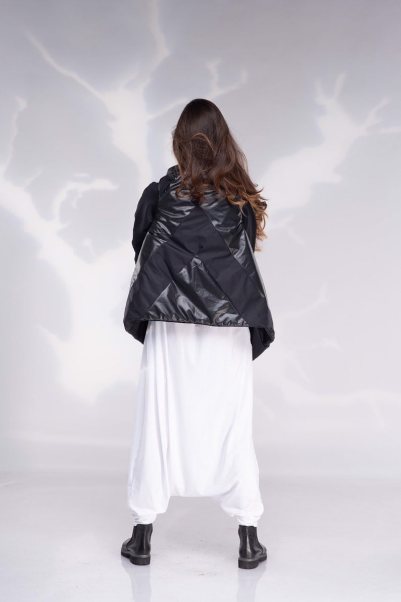 K&ouml;nnte beinhalten: Eine schwarze gesteppte Weste mit Rautenmuster. Die Weste wird &uuml;ber einer wei&szlig;en Hose getragen.