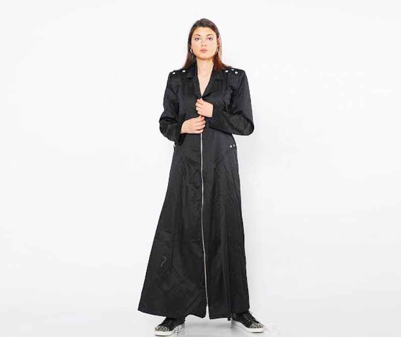 May include: A long black coat with a zipper closure and decorative buttons on the shoulders. The coat has a fitted bodice and a flowing skirt.