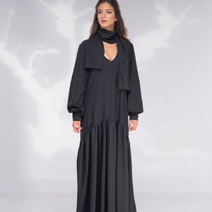 May include: A black maxi dress with long sleeves and a V-neckline. The dress has a tie at the neck and a ruffled hem.