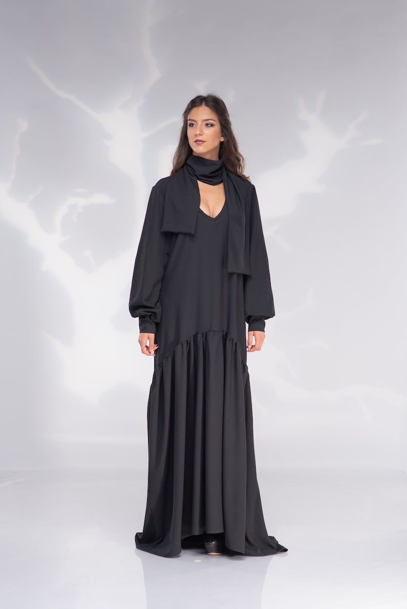 May include: A black maxi dress with long sleeves and a V-neckline. The dress has a tie at the neck and a ruffled hem.