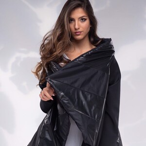 K&ouml;nnte beinhalten: Eine schwarze gesteppte Jacke mit hohem Kragen und einem langen, flie&szlig;enden Design. Die Jacke ist aus einem gl&auml;nzenden, wasserabweisenden Material gefertigt.