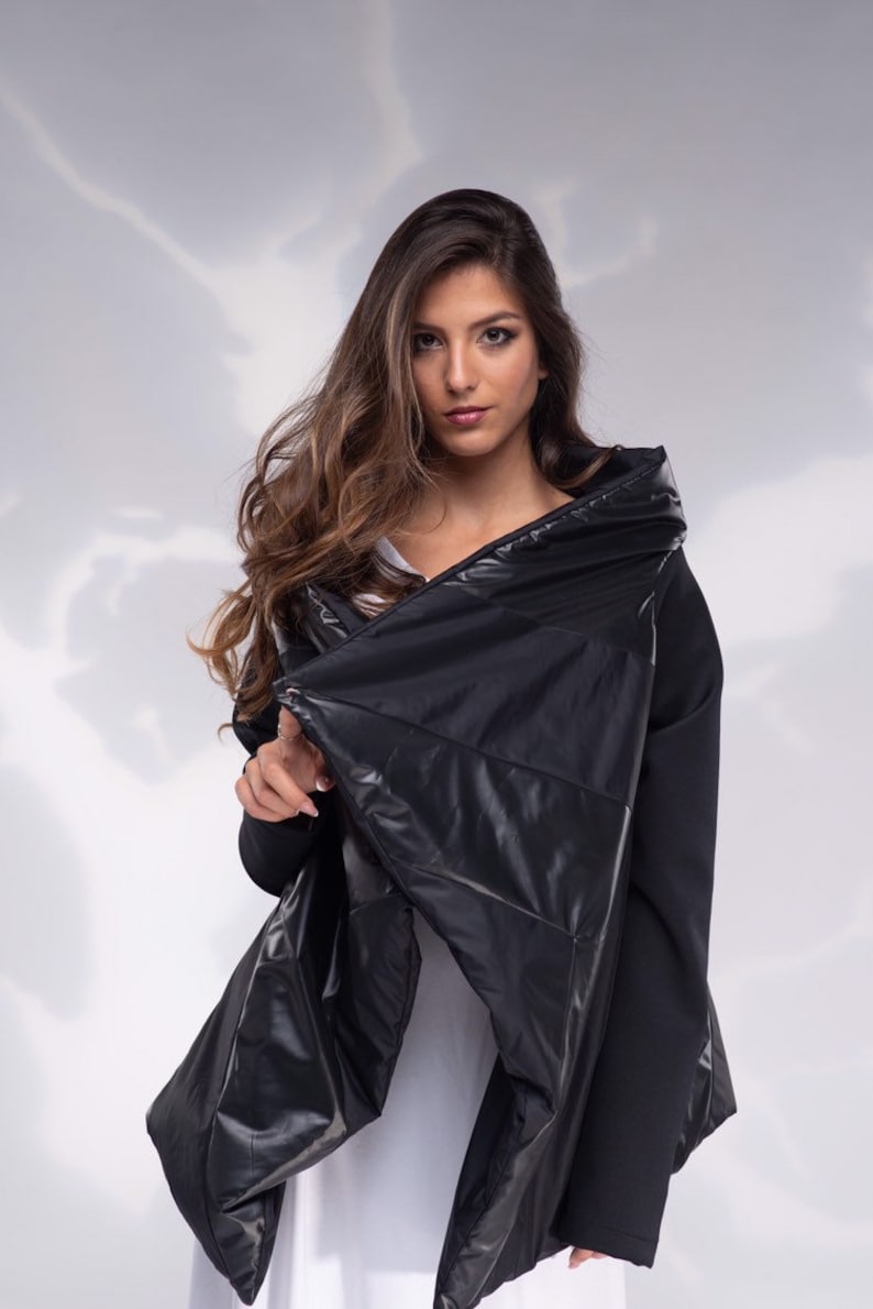 K&ouml;nnte beinhalten: Eine schwarze gesteppte Jacke mit hohem Kragen und einem langen, flie&szlig;enden Design. Die Jacke ist aus einem gl&auml;nzenden, wasserabweisenden Material gefertigt.
