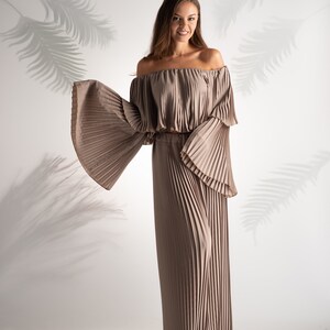 May include: A woman wearing a light brown off-the-shoulder top and matching wide-leg pants. The top and pants are made of pleated fabric.