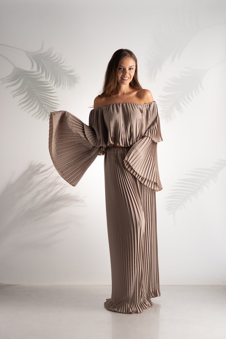 May include: A woman wearing a light brown off-the-shoulder top and matching wide-leg pants. The top and pants are made of pleated fabric.
