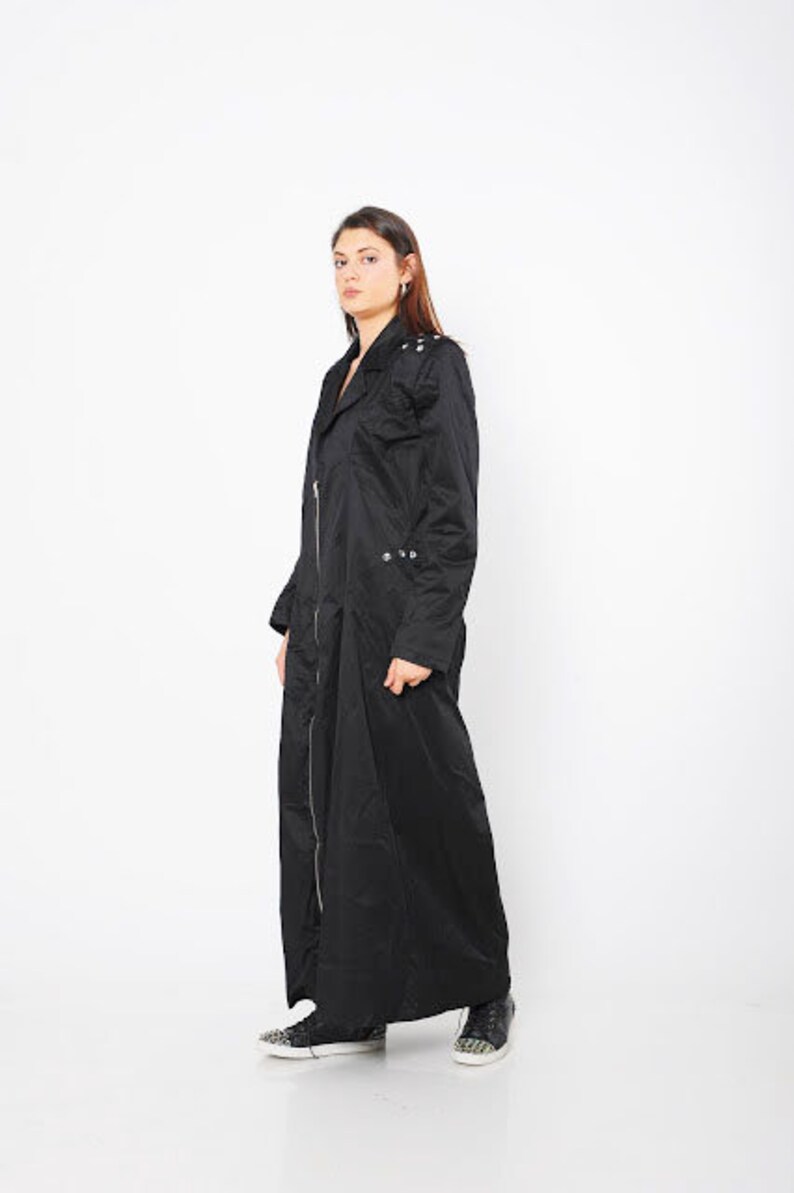 May include: A long black coat with a zipper closure and silver accents. The coat has a collar and long sleeves.
