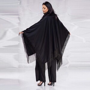 May include: A black fringed poncho with a long, flowing silhouette. The poncho is made of a soft, lightweight fabric and has a relaxed fit.