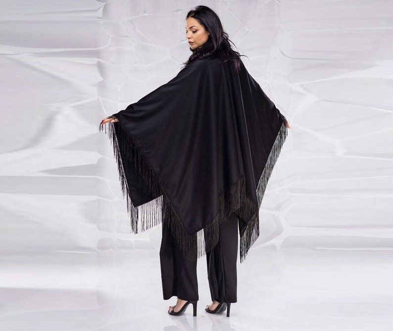 May include: A black fringed poncho with a long, flowing silhouette. The poncho is made of a soft, lightweight fabric and has a relaxed fit.