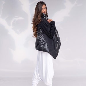 K&ouml;nnte beinhalten: Eine schwarz-wei&szlig;e Jacke mit hohem Kragen und einem langen, flie&szlig;enden Design. Die Jacke wird &uuml;ber einer wei&szlig;en Hose und schwarzen Stiefeletten getragen.