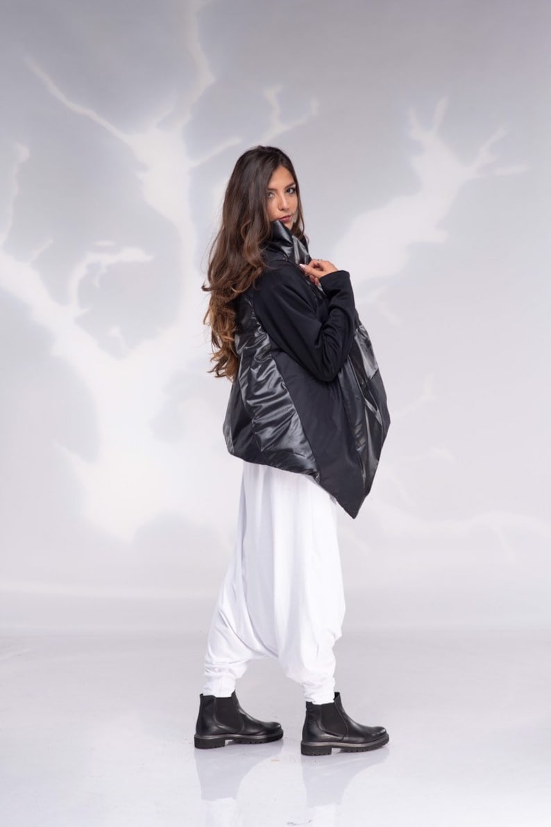 K&ouml;nnte beinhalten: Eine schwarz-wei&szlig;e Jacke mit hohem Kragen und einem langen, flie&szlig;enden Design. Die Jacke wird &uuml;ber einer wei&szlig;en Hose und schwarzen Stiefeletten getragen.