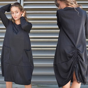 May include: A black long-sleeved dress with a gathered back and two pockets. The dress is made of a soft, stretchy fabric.