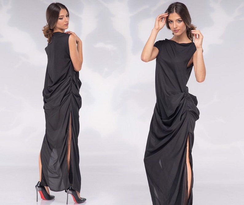 May include: A black sleeveless maxi dress with a draped, asymmetrical design. The dress features a high side slit and is paired with black high-heeled shoes. The fabric appears to be lightweight and flowing, creating an elegant silhouette.