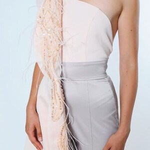 May include: A one-shoulder jumpsuit with a light pink top and a gray bottom. The top has a draped, feathered detail on one shoulder.