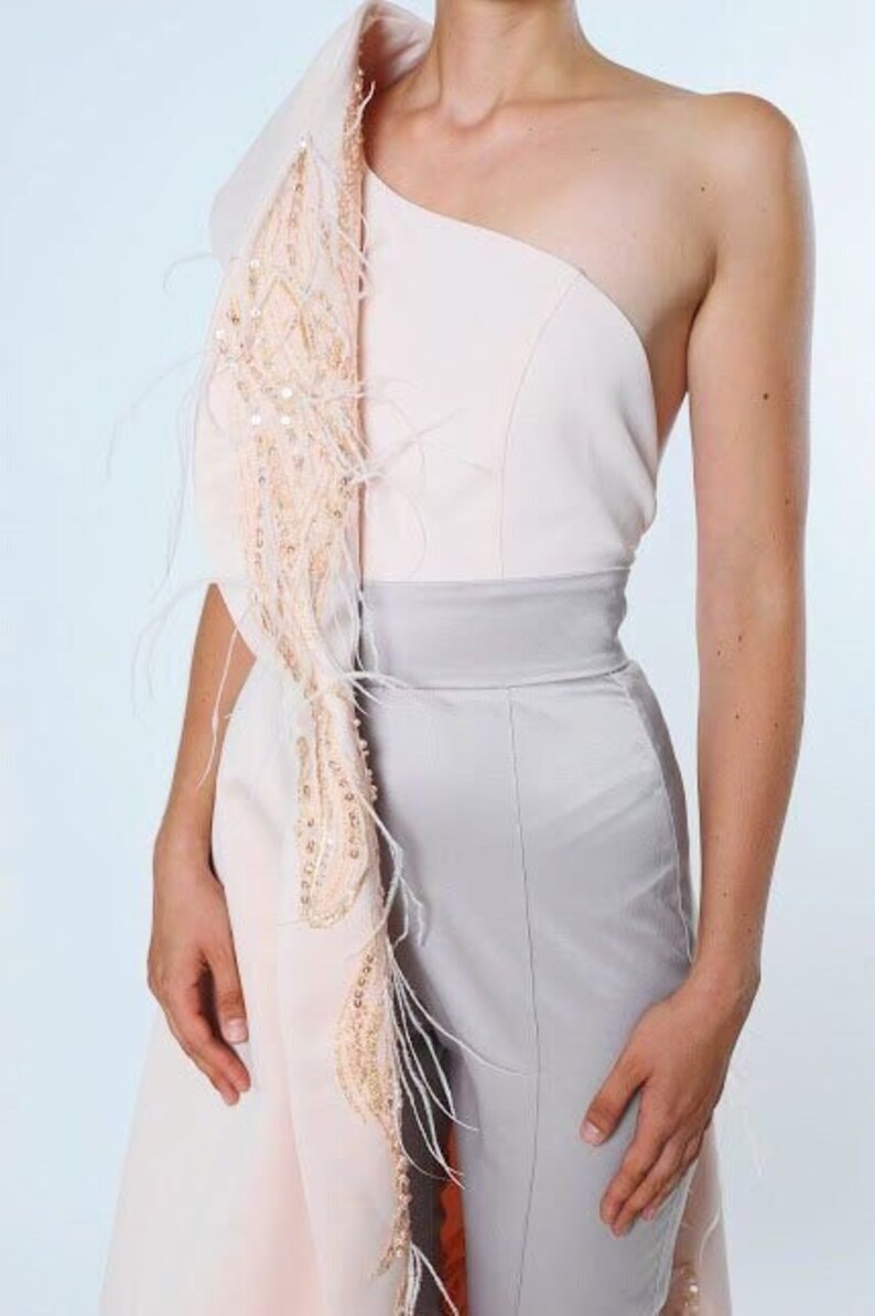 May include: A one-shoulder jumpsuit with a light pink top and a gray bottom. The top has a draped, feathered detail on one shoulder.