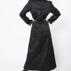 May include: A long black coat with a collar and long sleeves. The coat is made of a smooth fabric and has a straight silhouette.