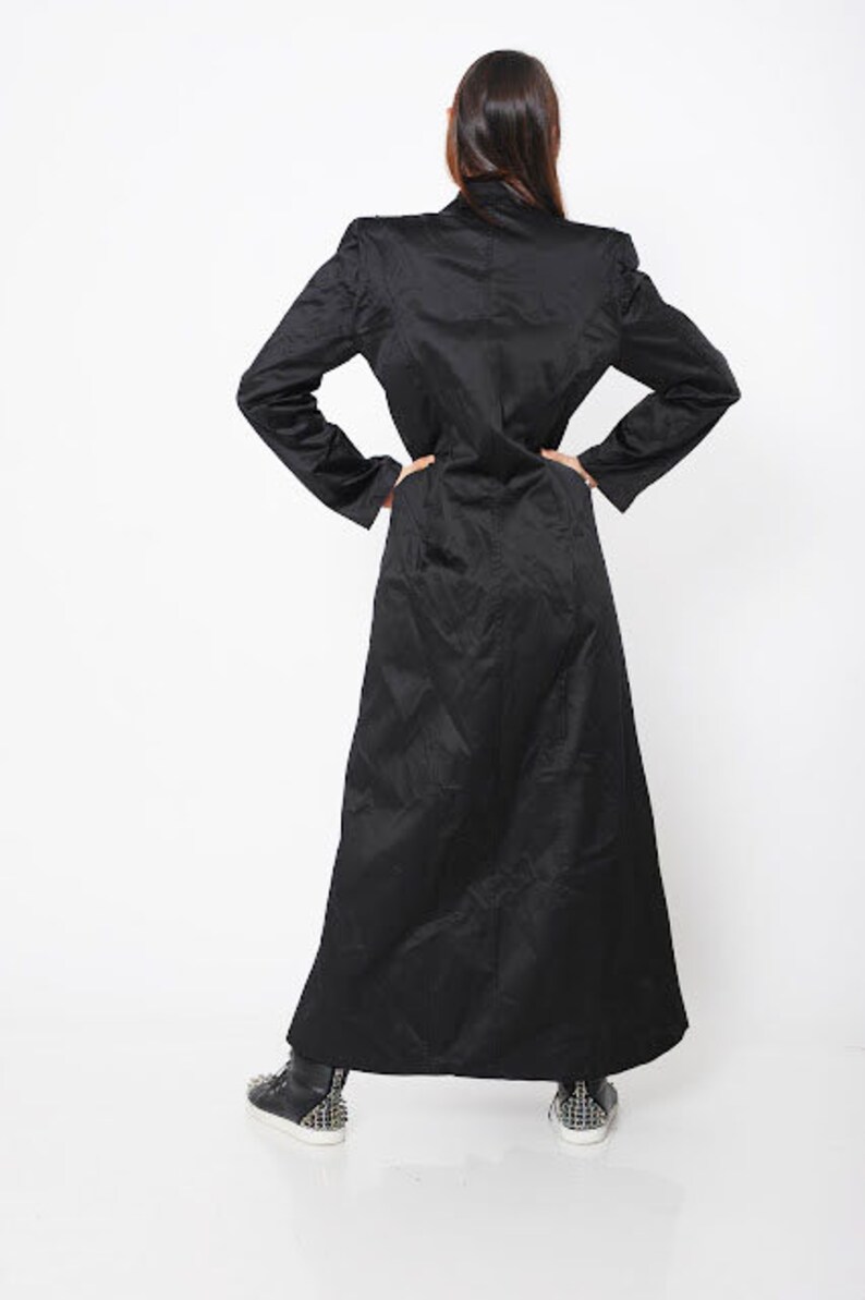 May include: A long black coat with a collar and long sleeves. The coat is made of a smooth fabric and has a straight silhouette.