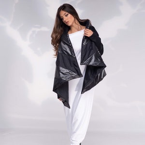 K&ouml;nnte beinhalten: Eine schwarze gesteppte Jacke mit einem langen, asymmetrischen Saum. Die Jacke hat eine Kapuze und wird &uuml;ber einem wei&szlig;en Oberteil und einer wei&szlig;en Hose getragen.