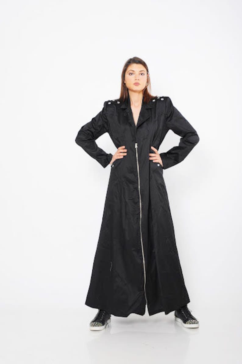 May include: A long black coat with a zipper closure and a stand-up collar. The coat has a slightly flared silhouette and is made of a smooth, lightweight fabric.