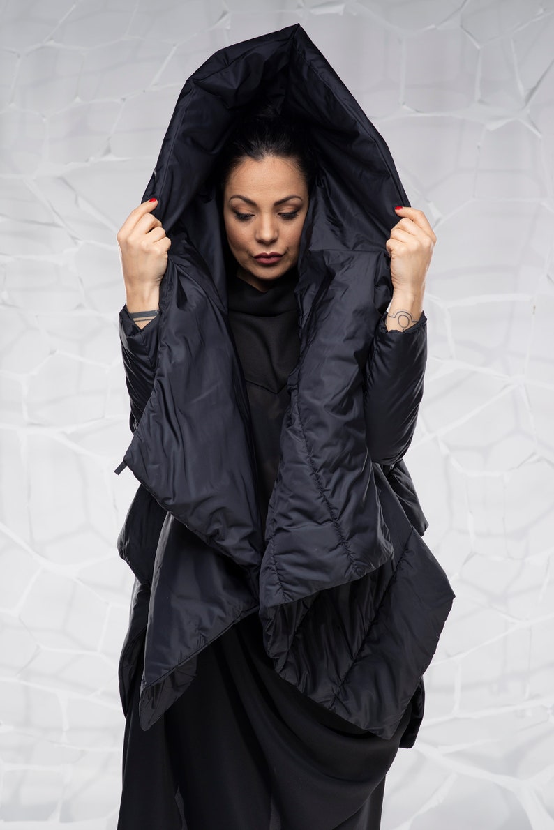 May include: A black hooded puffer jacket with a long, asymmetrical hemline. The jacket is made of a quilted fabric and has a relaxed fit.