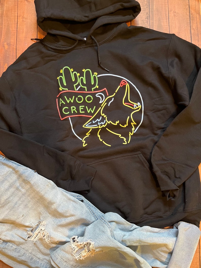 K&ouml;nnte beinhalten: Schwarzer Hoodie mit einem neon-gr&uuml;nen, gelben und roten Grafik eines heulenden Wolfes mit Kakteen und dem Text "AWOO CREW".