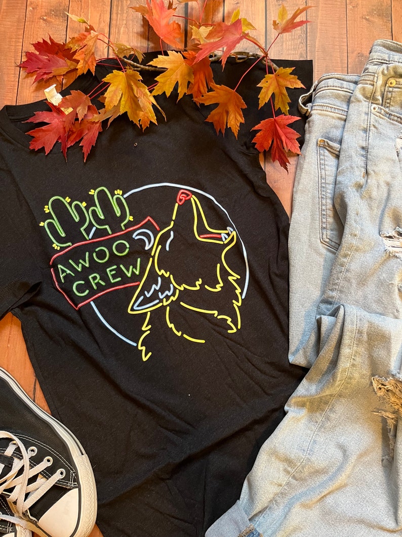 K&ouml;nnte beinhalten: Schwarzes T-Shirt mit einem neon-gr&uuml;nen, gelben und roten Grafik eines heulenden Wolfes mit Kakteen und dem Text "AWOO CREW".