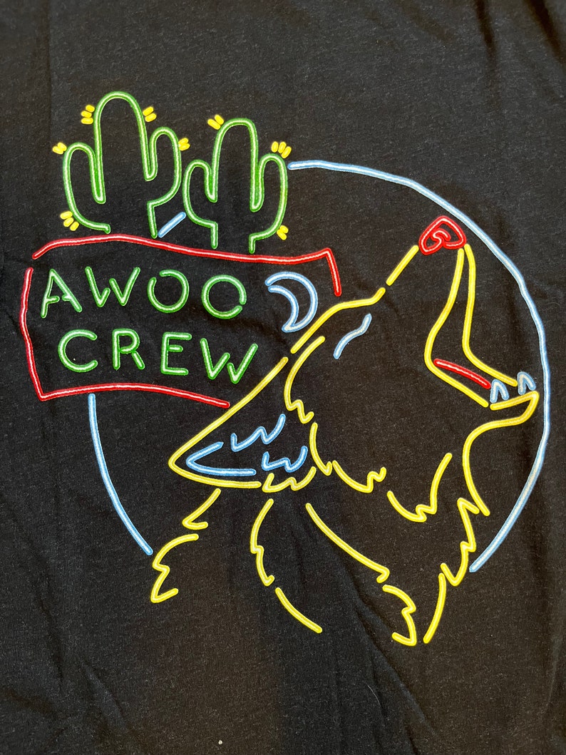 K&ouml;nnte beinhalten: Ein schwarzes T-Shirt mit einem neongr&uuml;nen, gelben und blauen Design eines heulenden Wolfes mit Kakteen und dem Text "AWOO CREW".
