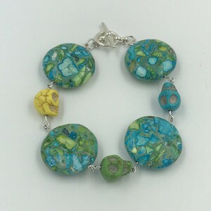 May include: A turquoise and green patterned bracelet with silver skull charms and a toggle clasp.