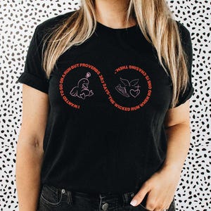 May include: Black t-shirt with a red graphic design featuring text and illustrations. The text reads "I wanted to go on a run but Proverbs 28:1 says the wicked run when no one is chasing them." The model is wearing size M.