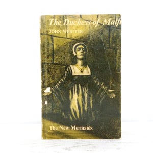 May include: A paperback book titled The Duchess of Malfi by John Webster from The New Mermaids series. The cover features a dark, olive-toned illustration of a person in a period gown with arms outstretched against a textured stone wall background.