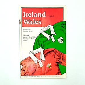 Puede incluir: Programa de partido de rugby vintage de Irlanda contra Gales. La portada tiene un encabezado rojo con el texto "Ireland Wales" y la fecha "23 de enero de 1982". El programa muestra camisetas de rugby verdes y rojas.