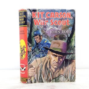 May include: Vintage book titled "Kit Carson, War Scout" by John Robb. The cover features illustrations of two men in military attire, one holding a gun. The spine is red with the title and author's name. The book is part of the Seagull Library.