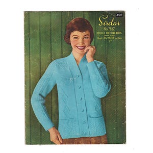 May include: Vintage knitting pattern cover featuring a woman wearing a light blue cardigan. The cardigan has a V-neck, button closure, and textured knit details. The cover includes the brand name "Sirdar" and text indicating the pattern is for double knitting wool, with bust sizes 34/36/38 inches.