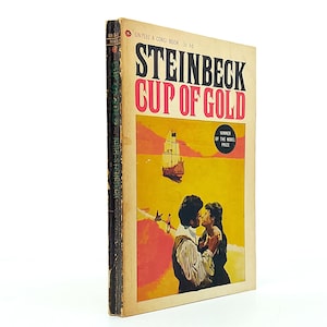 Op de afbeelding: Vintage paperback boekomslag voor "Cup of Gold" van John Steinbeck. De omslag heeft een gele en oranje achtergrond met een schip dat op zee vaart. De titel staat in grote rode en zwarte letters, met een kussend stel op de voorgrond.