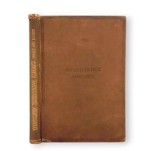 Puede incluir: Un libro marrón vintage titulado "Quantitative Analysis" con letras doradas. El lomo muestra el título "Elementary Quantitative Analysis" y el nombre del autor, "Wells and Bauser". El libro tiene un aspecto desgastado y envejecido.