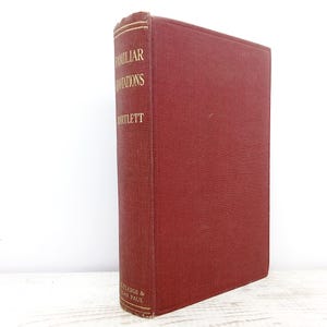 Könnte beinhalten: Ein rotes Hardcover-Buch mit dem Titel "Familiar Quotations" und dem Namen des Autors, Bartlett, in goldener Schrift auf dem Buchrücken. Das Buch steht aufrecht vor einem weißen Hintergrund.