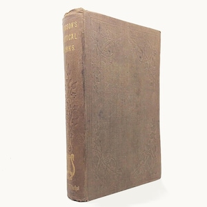 May include: A brown hardcover book with a textured fabric cover featuring embossed floral patterns. The spine displays gold lettering that reads "SON'S POETICAL WORKS" and includes a small gold lyre icon at the bottom, with visible wear on the edges.