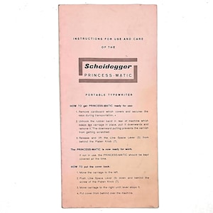 May include: A vintage instruction manual for a Scheidegger Princess-Matic portable typewriter. The manual is pink with black text, including instructions for use and care. The Scheidegger logo is prominently displayed.