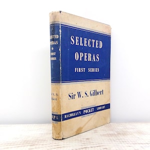 May include: A vintage book titled "Selected Operas First Series" by Sir W. S. Gilbert. The book has a blue spine and a blue panel on the cover with white text. The rest of the cover is a cream color. The book is part of the Macmillan's Pocket Library.