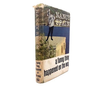 Puede incluir: Libro de tapa dura vintage titulado "a funny thing happened on the way" de Nancy Spain. La portada presenta a una mujer con sombrero y un paisaje. La columna vertebral del libro dice "NANCY SPAIN".