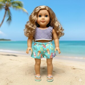 May include: A doll wearing a gingham crop top and turquoise shorts patterned with colorful flip-flops. The doll has blonde curly hair and is wearing matching flip-flops. The background shows a beach scene with a palm tree and ocean.