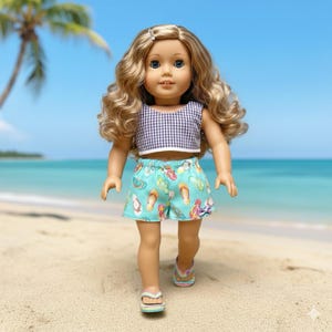 May include: A doll wearing a gingham crop top and turquoise shorts printed with colorful flip-flops. The doll has blonde curly hair and is standing on a sandy beach with a blue ocean and sky in the background.